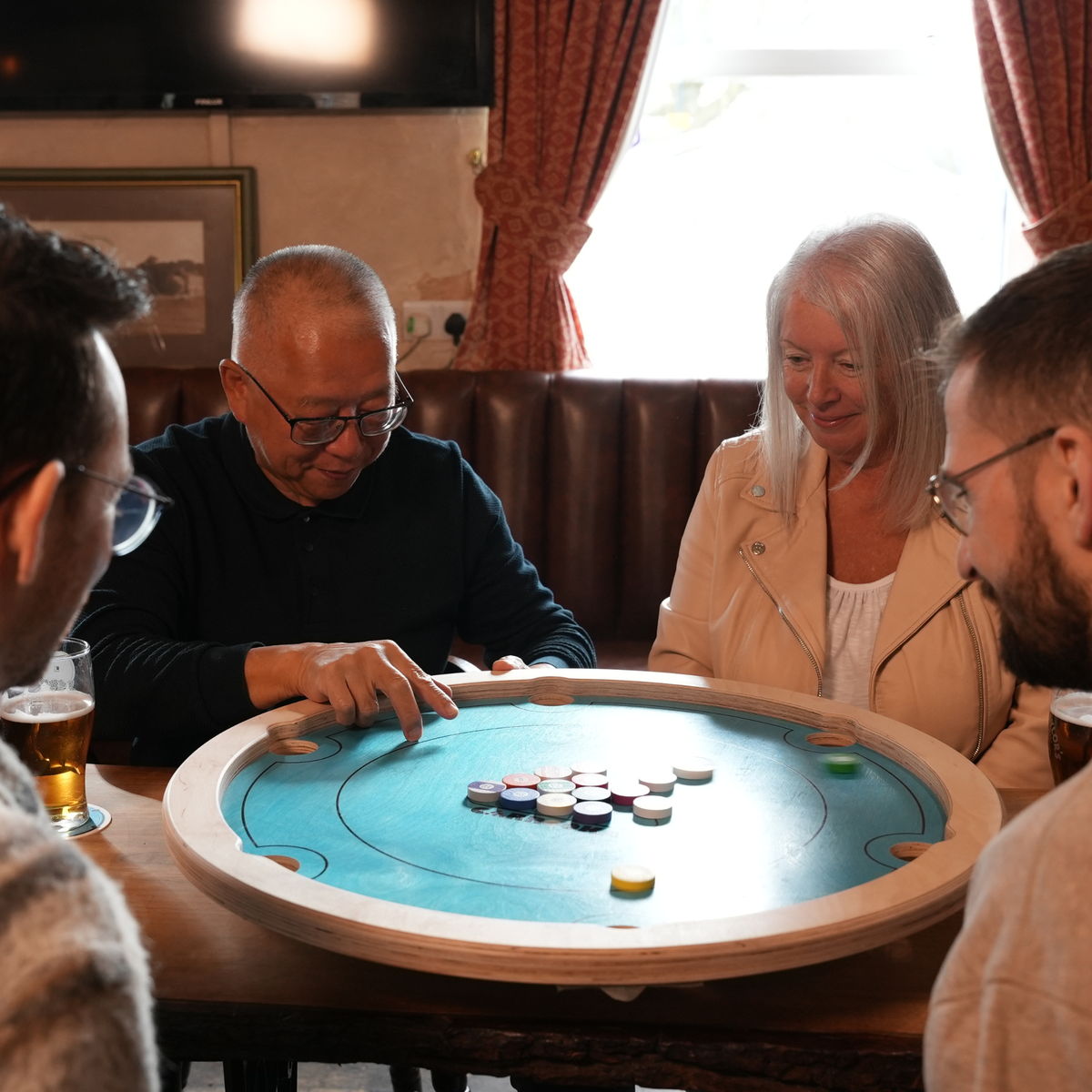 Vier Spieler rund um das Carrooka Pool 8 Blue Drehbrett an einem Pub-Tisch, ein Spieler bereitet seinen Stoß vor