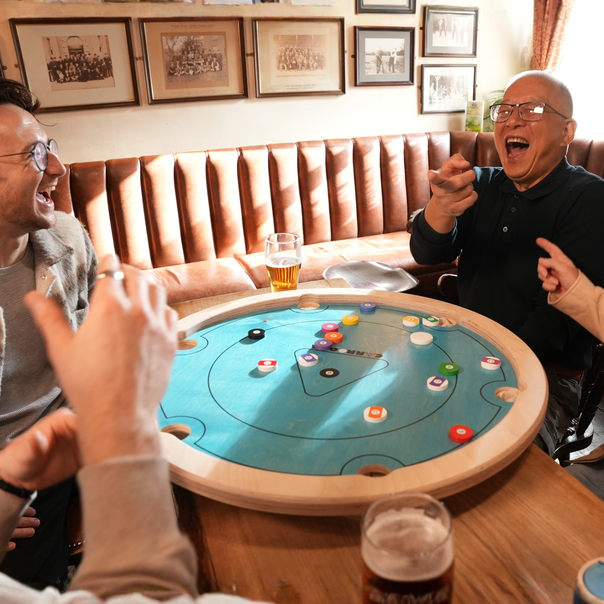 Freunde lachen bei einer Partie Carrooka Pool 8 Blue an einem Tisch im Pub
