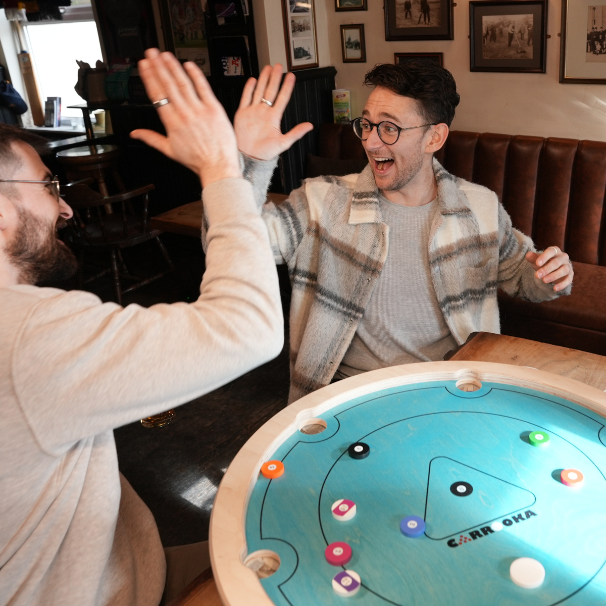 Zwei Spieler geben sich ein High Five über dem Carrooka Pool 8 Blue Drehbrett in einem Pub